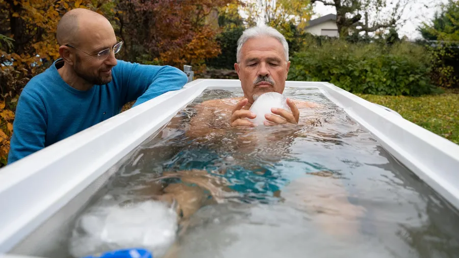 Coach unterstützt Teilnehmer beim Eisbaden und Mentaltraining in einer weißen Wanne im Garten