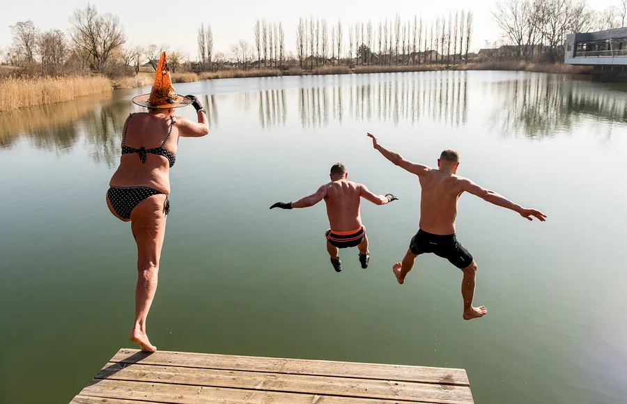 Drei Teilnehmer springen beim Eisbaden und Kältetraining gemeinsam von einem Steg in einen See