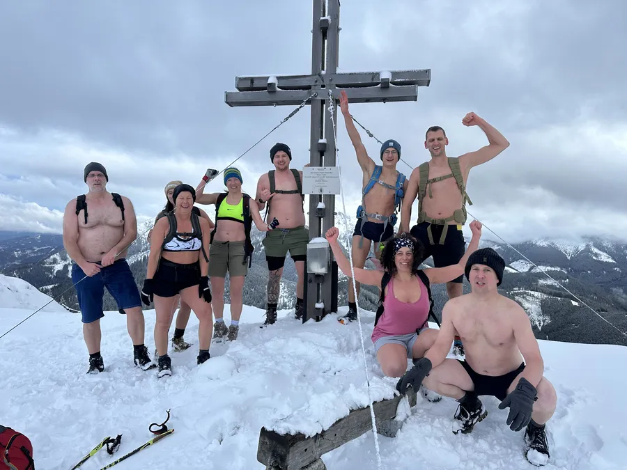 Groß (Tirol-Krampen-Wasserfall_Kreis_Eisbad_Jubel 01) Teilnehmer beim Mentaltraining Retreat Österreich feiern in Badekleidung am verschneiten Gipfelkreuz nach dem Kältetraing