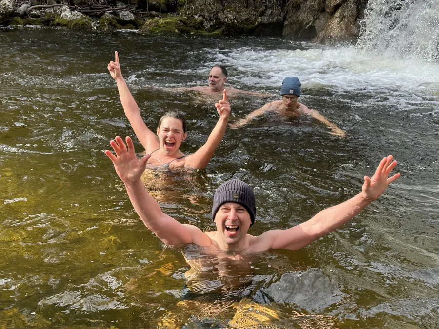 Glückliche Teilnehmer beim Eisbaden und Kältetraining in einem Fluss in Österreich mit Wasserfall im Hintergrund