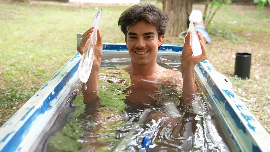 Lächelnder Teilnehmer beim Eisbaden und Mentaltraining hält Eisschollen in die Höhe