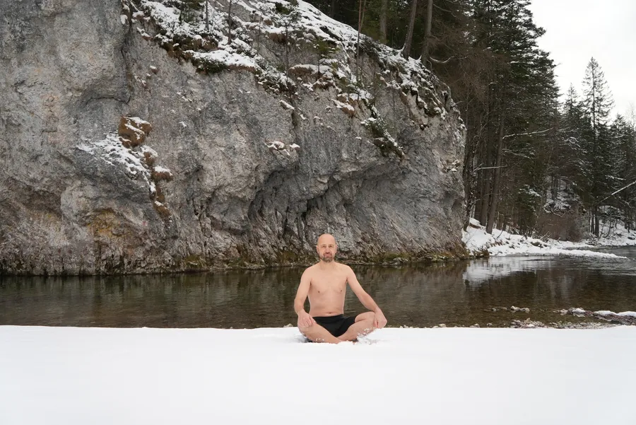 Mentaltrainer Marcus Bernhardt sitzt im Schneidersitz im Schnee vor einem Fluss - Kältetraining und Resilienz Coaching