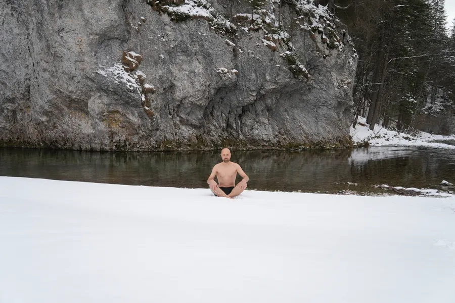 Mentaltrainer Marcus Bernhardt sitzt im Schneidersitz im Schnee am Flussufer beim Kältetraining und Resilienz Coaching