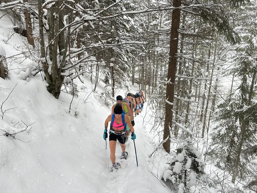 Gruppe beim Kältetraining und Eisschwimmen Retreat Steiermark wandert leicht bekleidet durch verschneiten Wald