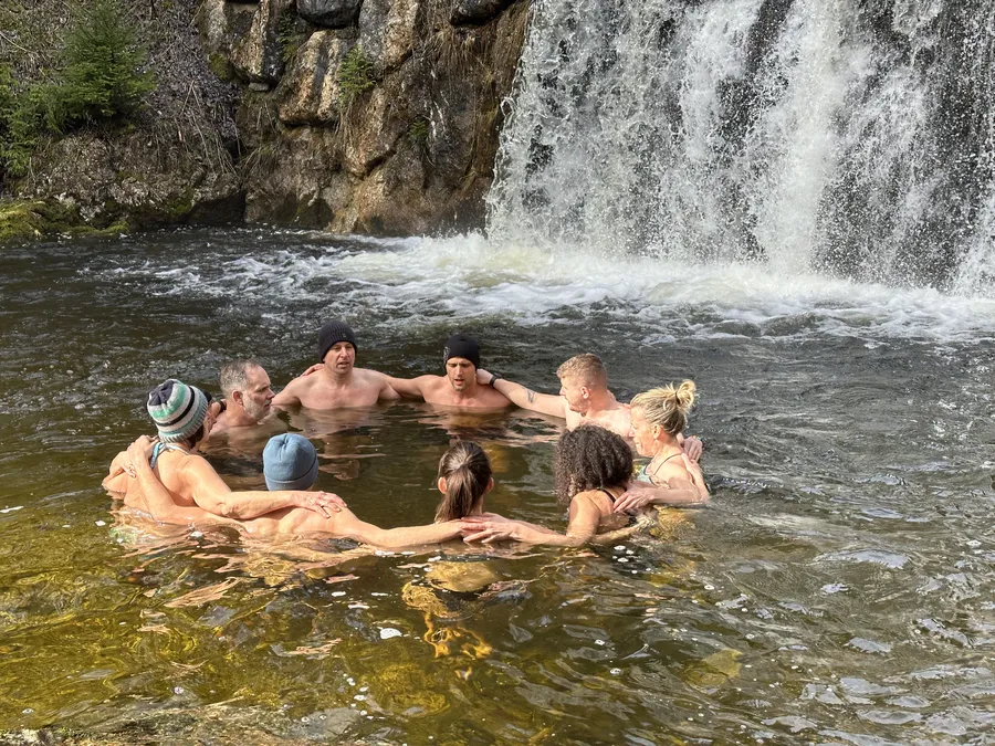 Gruppe beim Eisbaden und Kältetraining im Kreis vor einem Wasserfall während einem Mentaltraining Retreat Österreich